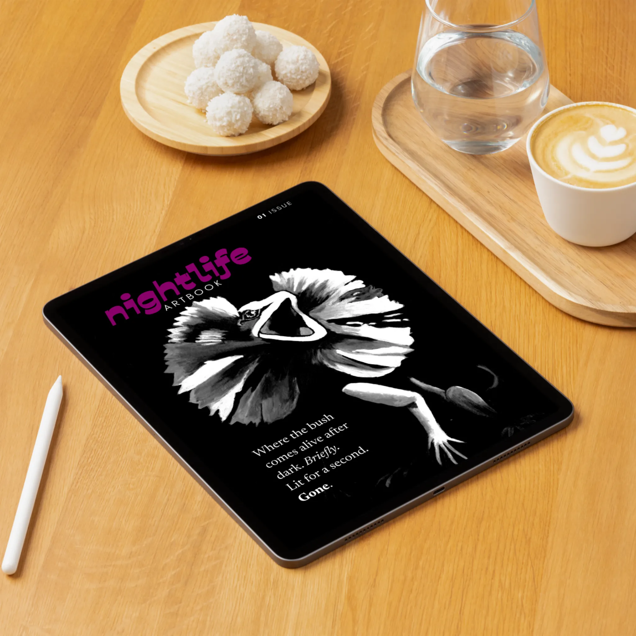 Nightlife Art Book issue 1 cover shown on a tablet, featuring the frilled-neck lizard painting All Talker, resting on a wooden desk